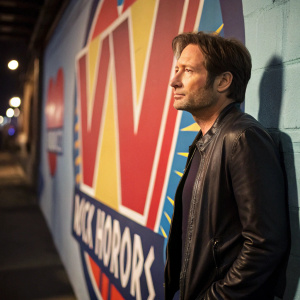 David Duchovny, sporting a serious expression, at the VH1 Rock Honors event. Beside him is a vibrant backdrop featuring the VH1 logo.