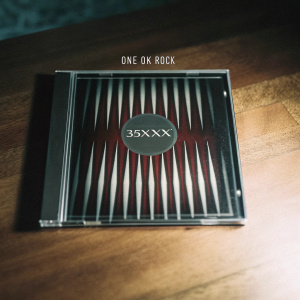 Music album '35XXXV' by One Ok Rock. Album cover with deep red background and sharp black and white patterns. CD in protective case.