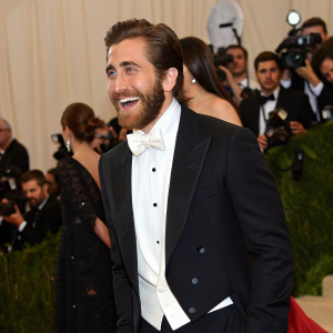 Jake Gyllenhaal at the Met Gala. Wearing an elegant tuxedo, a vibrant expression, surrounded by celebrities and paparazzi.
