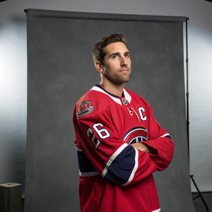 Chris VandeVelde, professional hockey player, standing confidently in a studio. Wearing a red NHL jersey with team patches. Gray backdrop