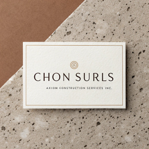 Business card design for Chon Surls at Axiom Construction Services Inc. Sleek, modern layout. Includes contact info, services list. Speckled earth-toned background.