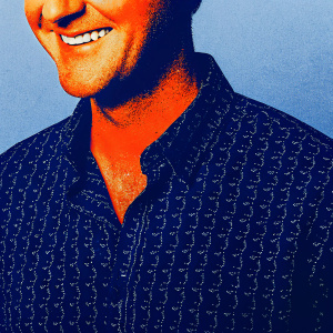 Tom Felton, Caucasian male, friendly smile. Wearing a patterned shirt, solid blue background. High-resolution close-up.