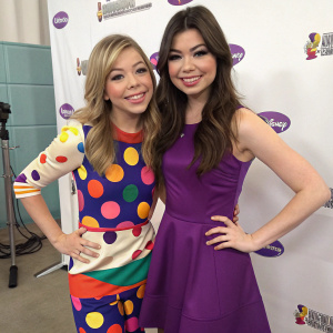 Jennette McCurdy and Miranda Cosgrove posing for a candid shot at a studio. Jennette in a playful, multicolored outfit, Miranda in a sleek purple dress. White backdrop with promotional logos.