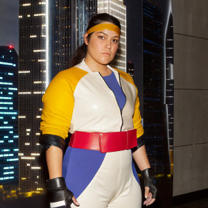 Motoko Kusanagi, cyborg heroine from Ghost in the Shell, depicted in sleek combat gear and a headband. Standing confidently in a futuristic urban landscape, surrounded by towering skyscrapers and neon lights.