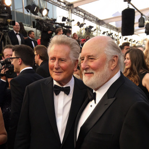 Martin Sheen and Rob Reiner, both in formal wear, at a Hollywood award show. Crowded event with flashing cameras