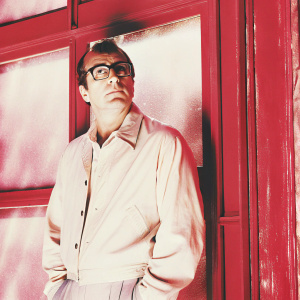 Martin Scorsese, with glasses, standing in front of a vibrant yellow backdrop. Serious expression.