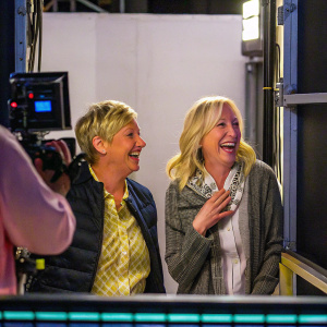 Ellen DeGeneres and Anne Heche laughing on set. Studio environment with minimal background