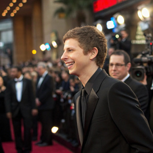 Michael Cera, smiling, at a Hollywood gala. Wearing a sleek black suit. Flashing lights and crowd in the background