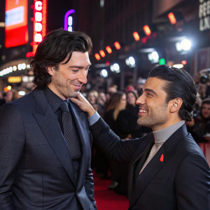 Adam Driver and Oscar Isaac at a bustling movie premiere. Driver adjusts his attire. Crowds and bright lights surround them.