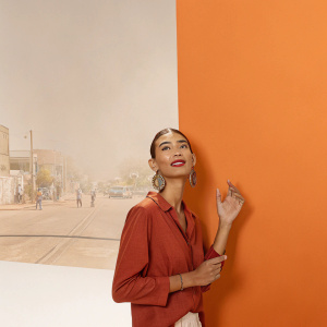 Pia Mia Perez, influencer, styled in a red blouse, posing on a sunny street. Lively street art in the background.