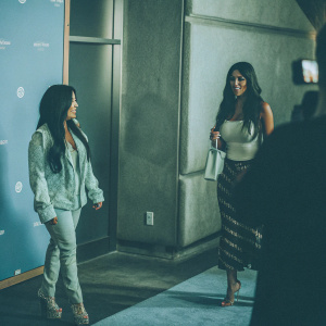 Jenni 'JWoww' Farley and Nicole 'Snooki' LaValle at the Universal Studios Hollywood event. Jenni in a light teal jacket, Nicole in a sleeveless top. Both have long dark hair and high-end fashion. Blue backdrop with Extra branding