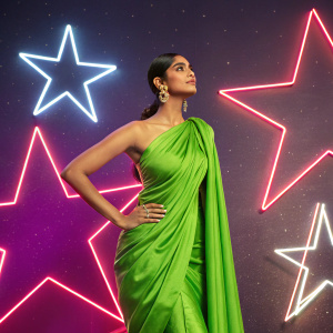 Bhumika Arora, an Indian model with a striking pose, wears a vibrant green sari. She stands against a neon-lit backdrop featuring a constellation of stars. The image highlights her modeling career achievements.