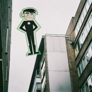 Danny Fenton in his Danny Phantom form, smiling confidently. He's got his signature black hair and ghostly green aura. Wearing a sleek black suit. Set against a stark white backdrop, the image is flat and cartoon-like.
