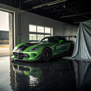Green and black Dodge Viper ACR Extreme parked in an open garage. Shiny black floor, fabric cover partially draped over the car