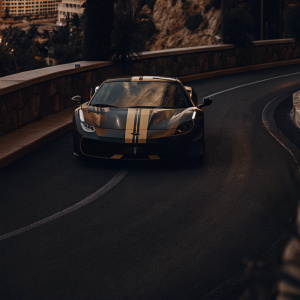 A Ferrari F8 Tributo racing on the winding roads of Monaco. The car is painted in a sleek matte black with yellow and blue racing stripes