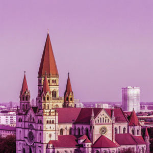 Aerial view of St. Francis of Assisi Church, located in bustling downtown Vienna. Gothic architecture, red rooftops, and towering spires stand out against a skyline dotted with modern skyscrapers.