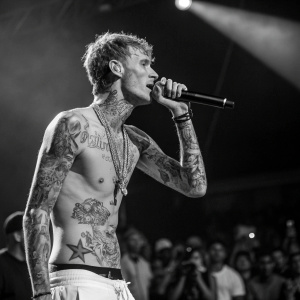 Machine Gun Kelly, shirtless on stage during live performance. Spotlight on his tattoos, crowd blurry in background