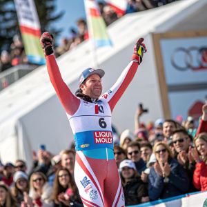 Beat Feuz, sponsored by LIQUI MOLY, stands atop the podium at the Audi FIS Alpine Ski World Cup Finals. Cheers from the crowd, blurry in the background.