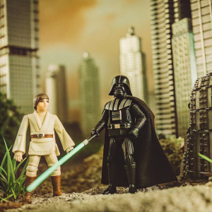 Darth Vader in an epic pose, standing beside a calm Luke Skywalker. Futuristic cityscape with tall metallic buildings. Dark and moody color palette. Star Wars themed diorama photo.