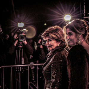 Gloria Allred and Mimi Haleyi standing together at the Women's Media Awards. Both women in elegant evening wear. Bright lights and media presence in background.