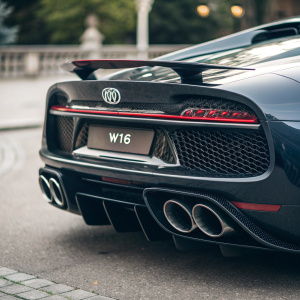 Close-up of a Bugatti Chiron, showcasing its sleek and luxurious design. Focus on the dual exhaust system, prominently displayed with distinctive design labels. Dark, sophisticated tones highlight the W16 logo-like emblem.