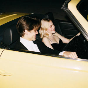 Oliver Cheshire and Pixie Lott enjoying a drive in a luxury sports car. Oliver is in a white shirt and black jacket, Pixie is in a black sequined dress. The modern car interior is sleek and dark-toned. The photo style is candid.