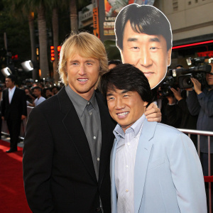 Owen Wilson and Jackie Chan at a Hollywood premiere. Owen Wilson holding a cardboard cutout of Jackie Chan's face. Red carpet with flashing cameras