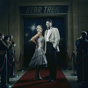 Katee Sackhoff and Karl Urban at a sci-fi gala. Dressed in elegant attire, standing on the vibrant red carpet with a massive Star Trek banner behind them.