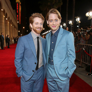 Seth Green and Macaulay Culkin in matching suits, standing at the entrance of a glamorous Hollywood awards show.