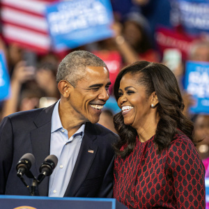 Former President Barack Obama and Michelle Obama, smiling, candid photo at political rally. Backdrop of enthusiastic crowd