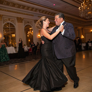 Laura Schirripa in a black gown, Steve Schirripa in a striped suit. They are dancing at a celebrity charity gala.