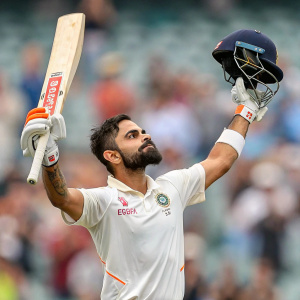 Virat Kohli, wearing white jersey with orange accents, celebrating his recent wicket. Out of focus stadium audience in the background.