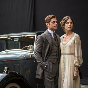 Zac Efron and Amanda Crew standing beside a vintage car. Dressed in period costumes. Dark studio backdrop.