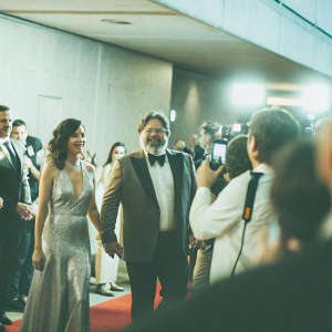 At a bustling awards show, Britney Theriot, Russell Crowe, and Roberto Gualtieri walk the red carpet. Surrounded by flashing cameras and curious onlookers.
