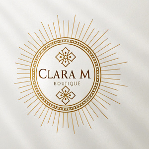 Elegant boutique logo. Gold emblem with cross pattern and radial lines on crisp white backdrop. Name 'CLARA M BOUTIQUE' integrated into design.