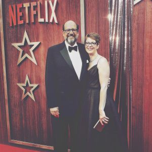 Fred Melamed and Leslee Spieler at the Netflix awards, posing against a backdrop of stars and Netflix logo. Both are dressed in formal attire.