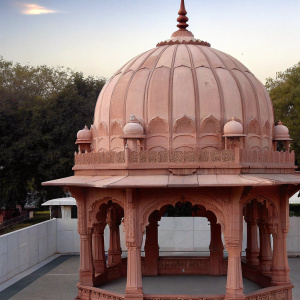 The majestic Boliya Sarkar ki Chhatri temple in Indore. Pinkish-orange dome with intricate carvings. Surrounded by lush greenery and traditional Indian temple architecture.