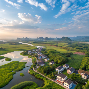 Aerial view of a serene town in Huixian National Wetland Park, Lingui, Guilin, China. Lush green landscapes, residential houses, and tranquil wetlands with clear water. Bright blue sky dotted with delicate clouds. Predominant hues of green and brown.
