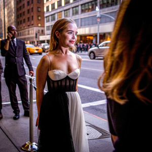 Emilia Clarke, donning a stunning black and white strapless gown, makes an appearance at the Gotham Awards. The backdrop is a bustling New York City street.