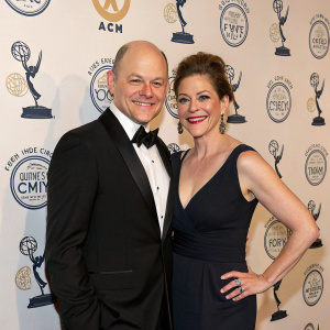 Rob Corddry and Sandra Corddry at a gala event, posing for a photo against a backdrop filled with comedic icons and award logos.