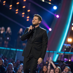 Michael Bublé, in a black suit, performing at the Grammy Awards. Vibrant stage lighting and enthusiastic crowd visible.
