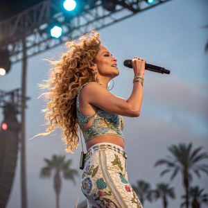 Jennifer Lopez, on stage at Coachella, holding a microphone. Curly hair, dynamic pose.