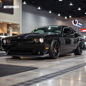 Motorprints logo in background, sleek black Dodge Challenger SRT8 parked. Aggressive stance, car show setting.