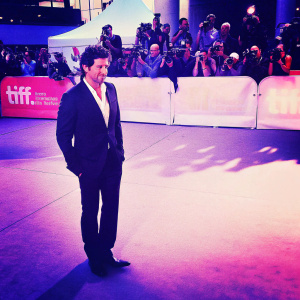 Patrick Dempsey, wearing a black suit and white shirt, at the Toronto International Film Festival. Surrounded by flashing cameras and paparazzi.