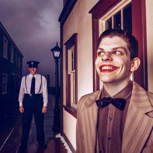 Promotional image for Gotham. Jerome Valeska, as the Joker, menacing grin. A police officer, grim expression. Dark, gloomy atmosphere. Black and red color scheme.