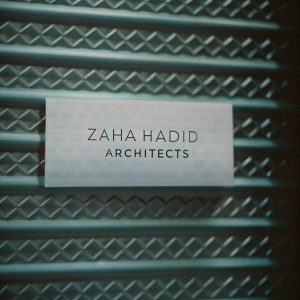 Business card for Zaha Hadid Architects. Sleek, modern design with metallic texture and repeating geometric patterns. Predominantly white with metallic accents and sans-serif font. Neutral gray background.