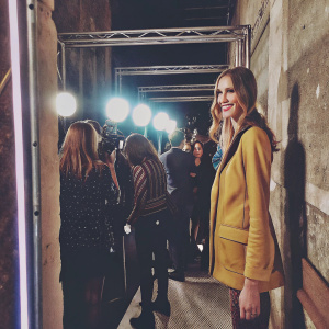 Chiara Ferragni, wearing a mustard yellow blazer, smiling. Crowded backstage area, photographers flashing lights