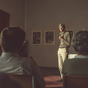 Arsene Wenger, dressed in casual attire, at a Q&A session. White walls and audience in background