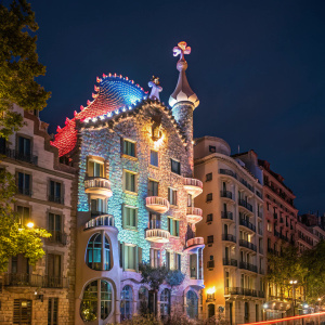 A stunning night scene of Casa Batlló in Barcelona, Spain. The iconic structure designed by Antoni Gaudí, illuminated with vibrant colors and unique shapes.