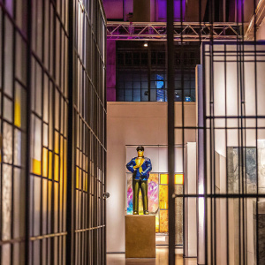 Josuke Higashikata from JoJo's Bizarre Adventure standing in a modern art gallery. Purple and yellow hues dominate the background, contrasting with his outfit.